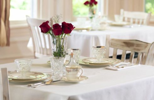 White covered dining tables set with white china and red roses.