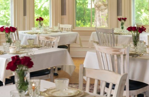 White airy dining room with tables set with white china and red roses