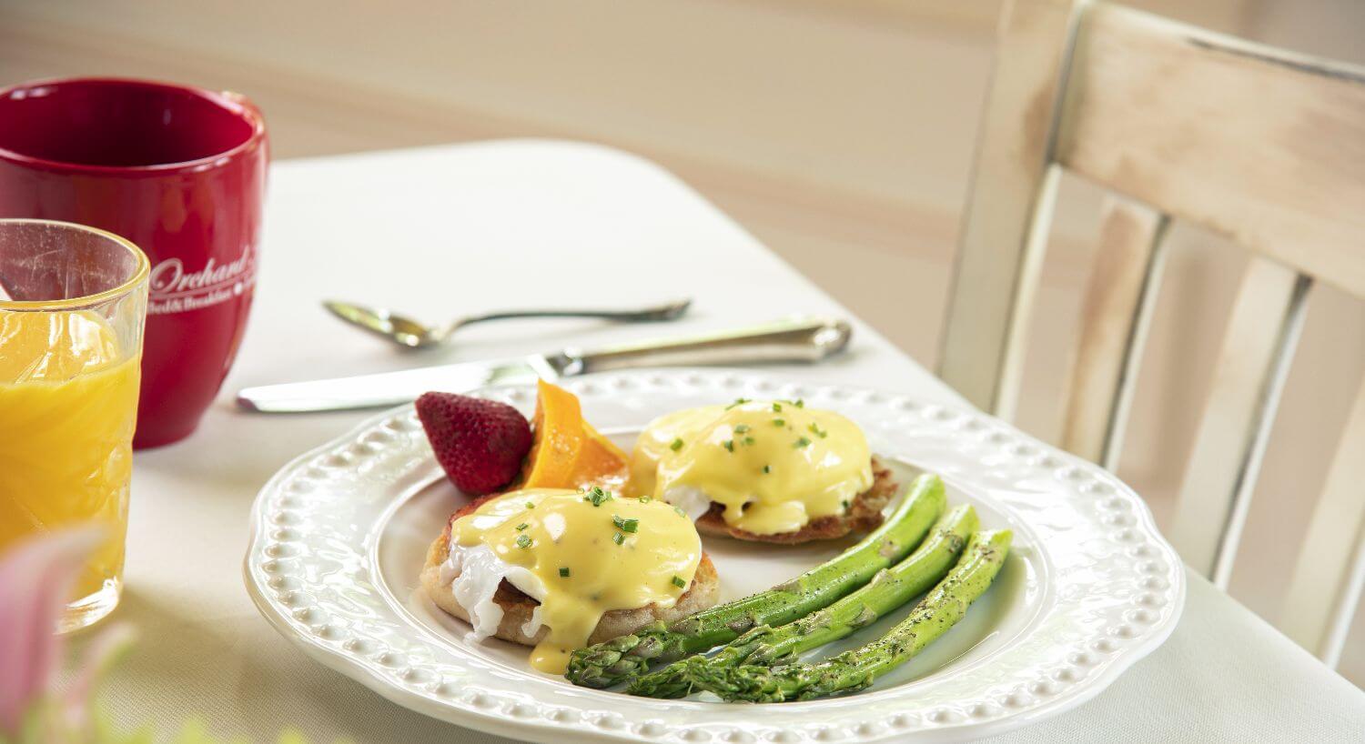 Eggs benedict served with asparagus on a white plate with fruit.