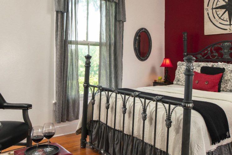 Large black bedstead in a room decorated in whtie with black and red touches.