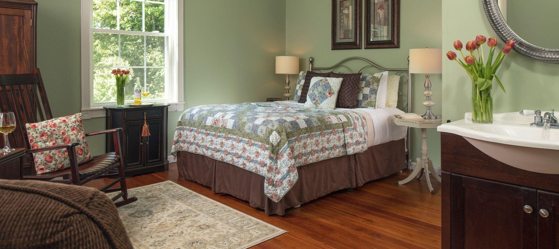Wood floors in a guest room with light green walls and large bed covered in a coordinating quilt.
