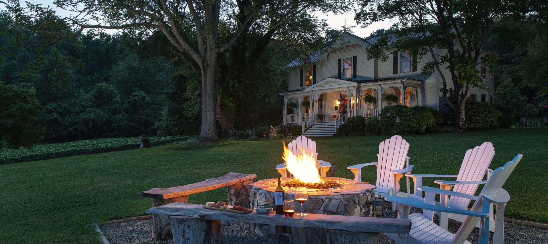Chairs around a fire pit on a green lawn outside a large white manor house