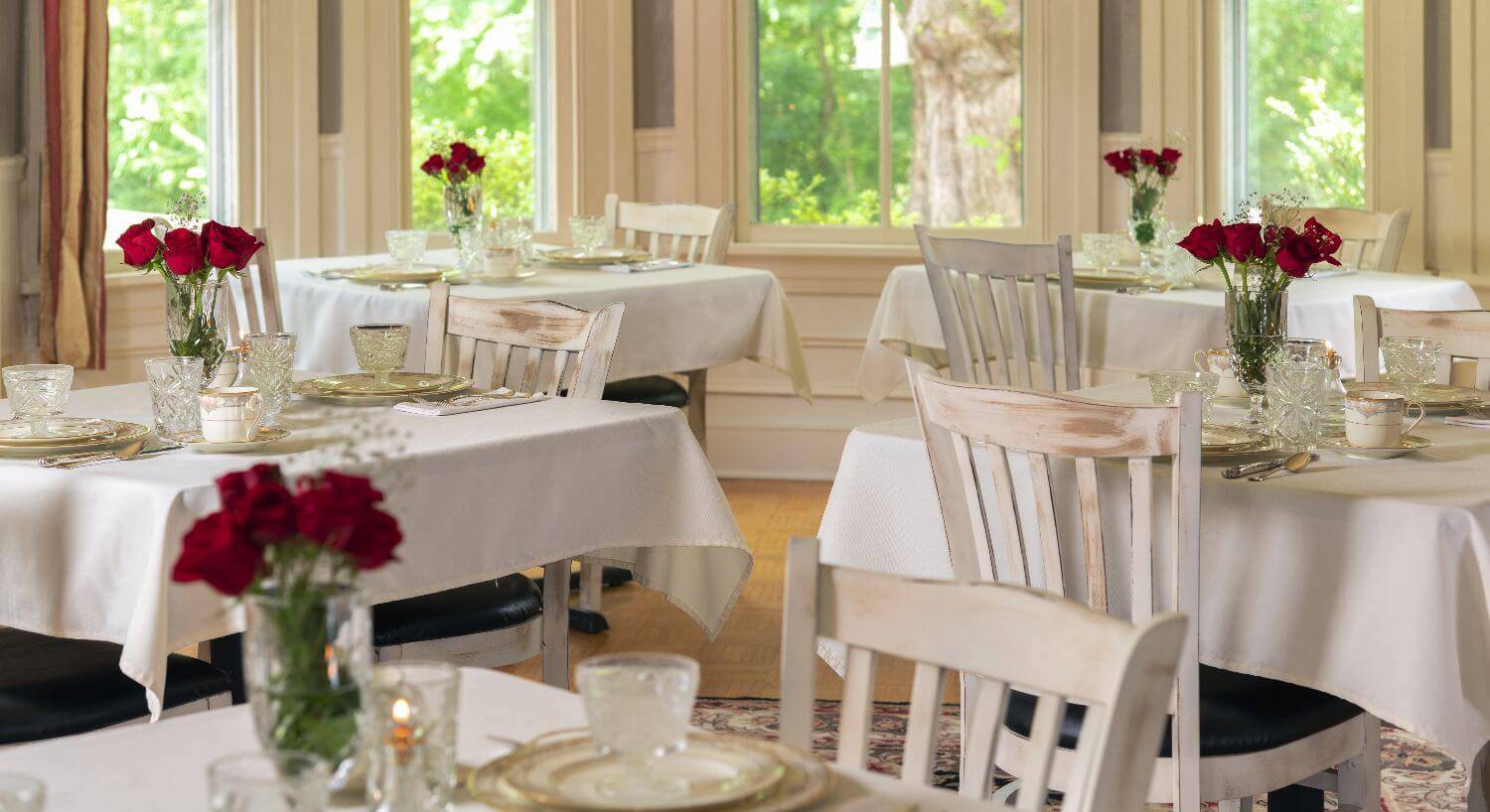 White airy dining room with tables set with white china and red roses