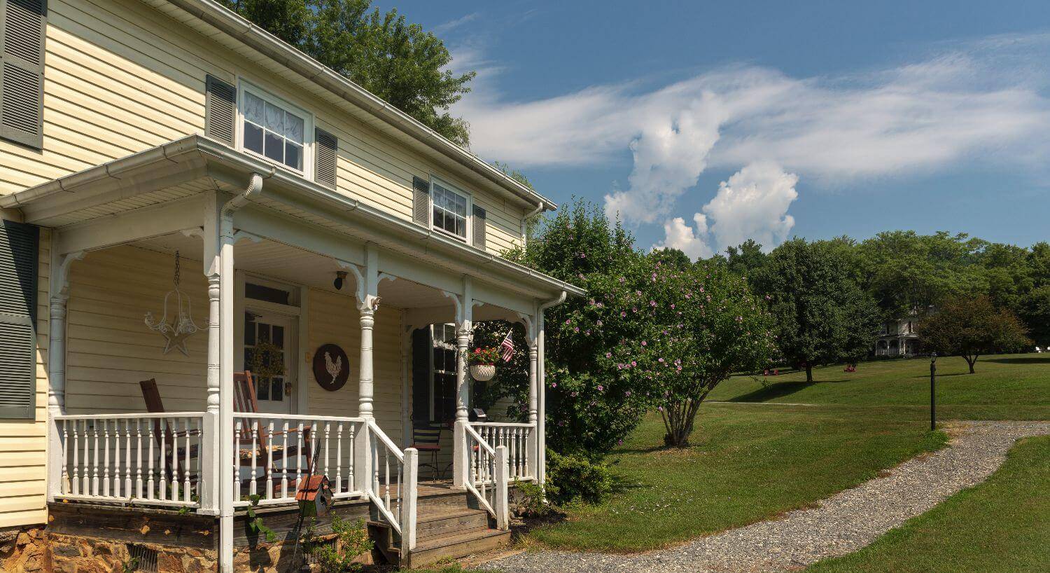 Yellow farmhouse with large porch set on green lawn and a rock path