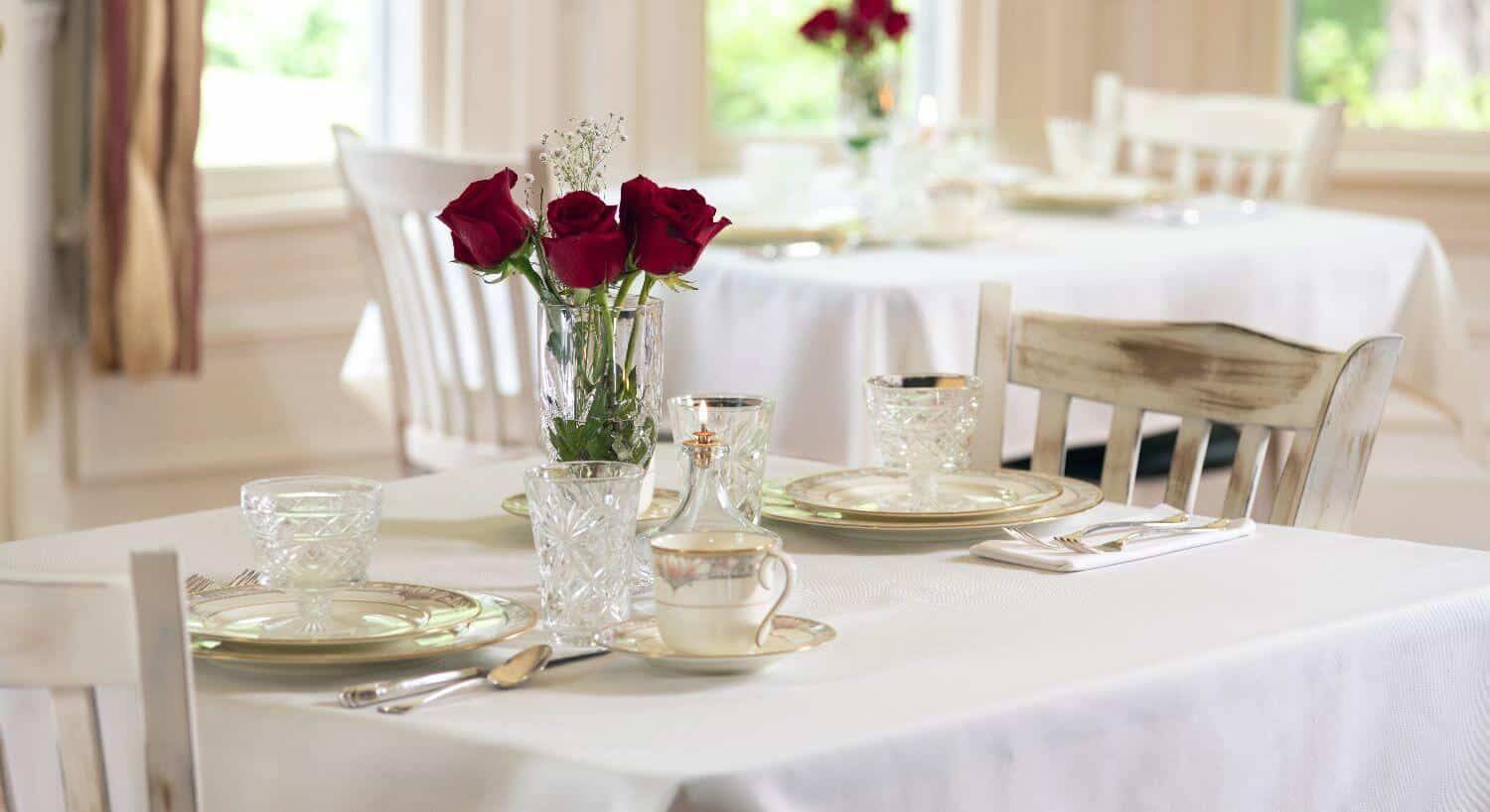 White covered dining tables set with white china and red roses.